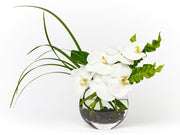 White orchids with accented greens in a clear oval vase