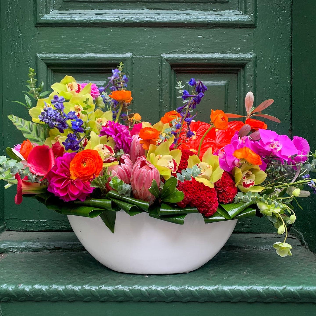 An electric colorful arrangement filled with orchids, delphinium, ranunculus, roses, anthurium, tropical flowers, calla lilly, and more!