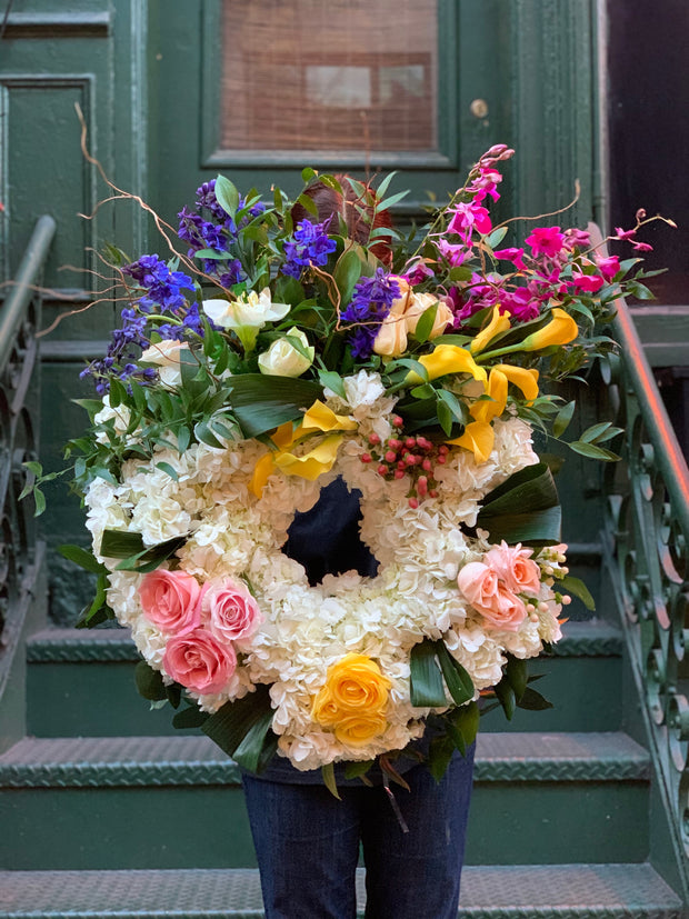 funeral wreath consists of blue delphinium, purple orchids, white hydrangea, colorful calla lilly, and rose accents