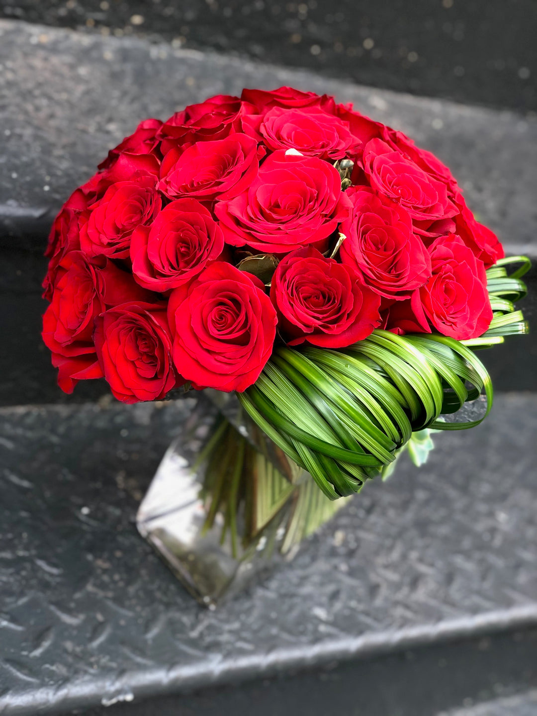 A Bouquet Style Rose Arrangement with Accents of Green Modern Leaf work and a succulent.