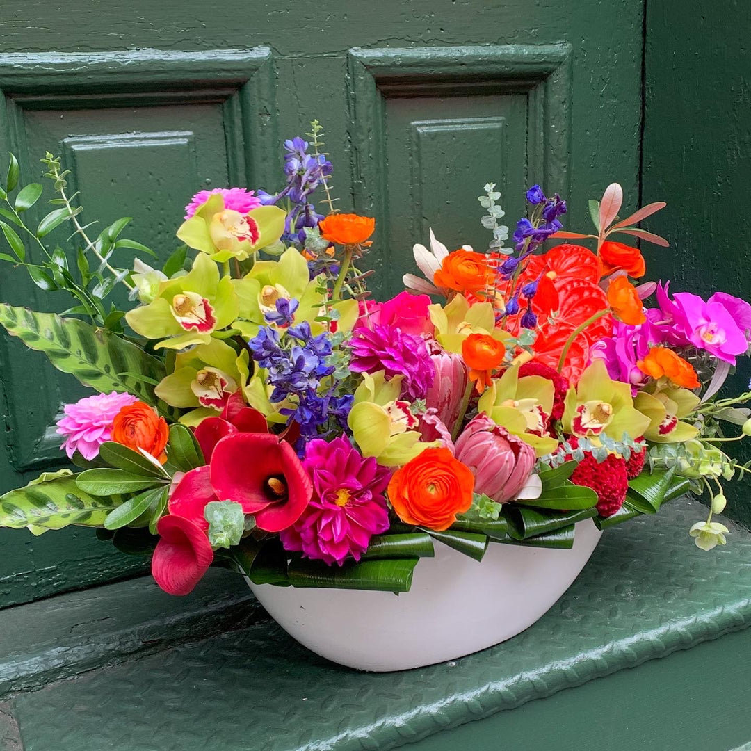 An electric colorful arrangement filled with orchids, delphinium, ranunculus, roses, anthurium, tropical flowers, calla lilly, and more!