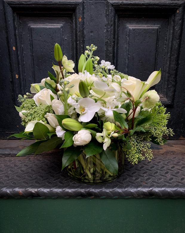 all white arrangement showing phalaeonopsis orchid heads, casablanca lilies, tulips, roses, laceflower, and garden greens